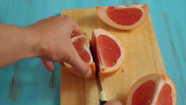 Cutting ripe grapefruit on board close-up. Citrus fruits, making fresh juice or tropical cocktails.