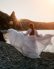 Fototapeta na wymiar Mysterious young woman with braids in long white dress alone on the beach. Sunset over the sea with rocky volcanic cliff. Abstract nature summer ocean sea background.