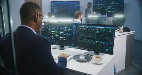 African American big data scientist works at computer in monitoring room. Multiracial colleagues...