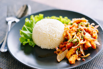 Spicy chicken salad with rice in a black plate with a spoon on the table.