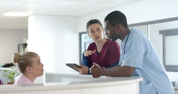Diverse doctors talking to medical recepcionist sitting at front desk at hospital, slow motion