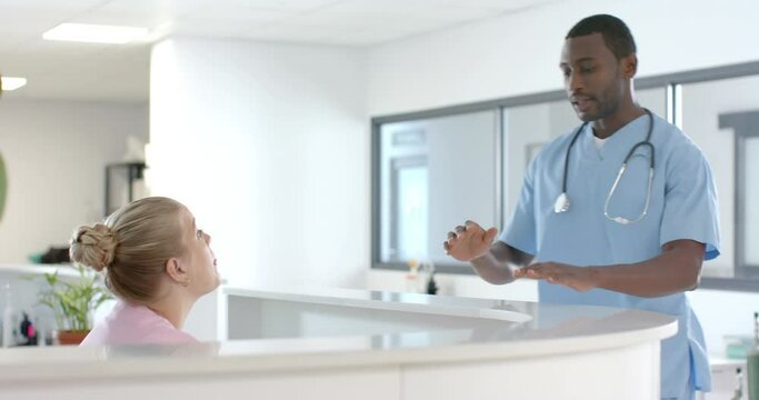 African american male doctor talking to medical recepcionist at front desk at hospital, slow motion