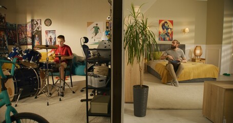 Young boy plays drum kit in bedroom. Male musician plays traditional djembe drum at home. View of...