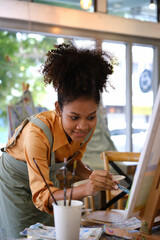 Talented African American female artist painting on canvas in art workshop. Art, creative hobby and...