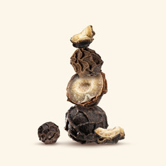Close-up of a stack of Organic dried black pepper seeds, whole and sliced peppercorn on a beige...
