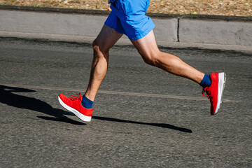 legs male runner running city marathon race, contrasting jogger shadow on asphalt road