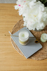 Home cozy interior. Candles, a bouquet of peonies in a glass vase, a glass of matchalate on a wooden coffee table. Spring.