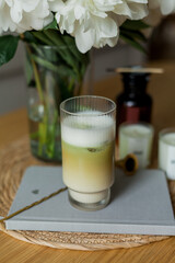 Home cozy interior. Candles, a bouquet of peonies in a glass vase, a glass of matchalate on a wooden coffee table. Spring.