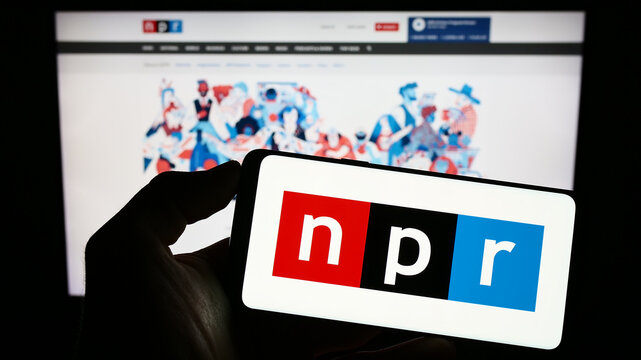 Stuttgart, Germany - 06-17-2023: Person holding cellphone with logo of media organization National Public Radio (NPR) on screen in front of webpage. Focus on phone display.