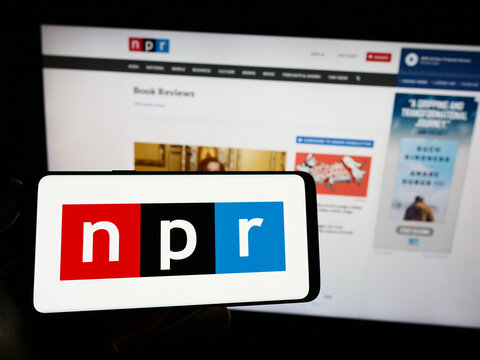 Stuttgart, Germany - 06-17-2023: Person holding mobile phone with logo of media organization National Public Radio (NPR) on screen in front of web page. Focus on phone display.