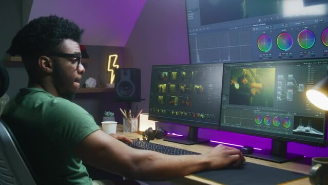 African American colorist edits action movie, makes color correction, works at home. Program interface with RGB tools and wheels on computer and big digital screen. Concept of film post production.