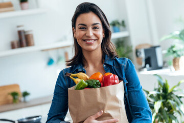 Happy beautiful woman holding cardboard bag with health shopping in kitchen at home