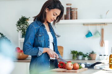 Healthy young woman cutting fresh vegetables while cooking healthy food in the kitchen at home.