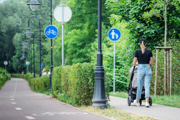 Young blonde hair girl with stroller walking near the bike road with blue road sign or signal of...