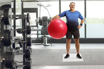 Fototapeta na wymiar Mature man with a fitness exercise ball standing in a gym