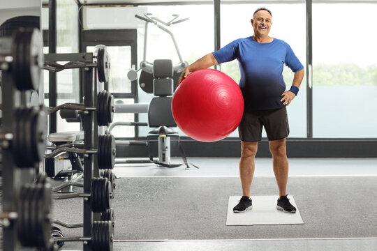 Mature Man With A Fitness Exercise Ball Standing In A Gym