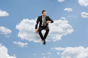 Businessman sitting on a cloud and checking time on watch