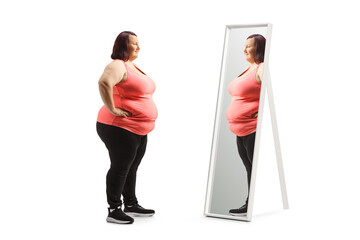 Full length profile shot of an overweight young woman in sportswear standing in front of a mirror
