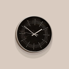 Abstract black wall clock on a beige wall with soft shadows.