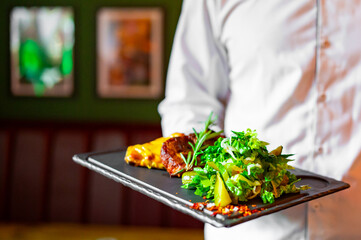 chef hold plate with grilled pork neck with baked potatoes and salad in cafe