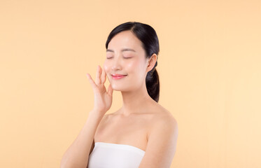 Naklejka premium Beautiful girl asian model touching fresh glowing hydrated facial skin on beige background closeup. Beauty face young woman with natural makeup and healthy skin portrait. Skin care concept