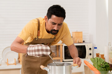 Asian man enjoy making main courses, Smart father is cooking pasta for his daughter in the morning. Happy man was boiling the soup and Stirring the boiling broth. Male preparing breakfast at home.