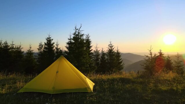 Hikers camping site on hillside at bright sunset. Tent shelter on mountain campsite on sunny evening. Active tourism and hiking concept