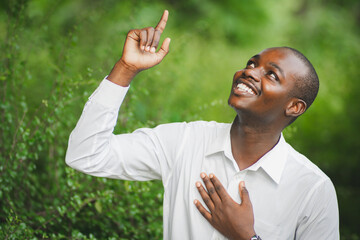 African man in white shirt hold hands on heart chest feel peace, happy thankful biracial male...