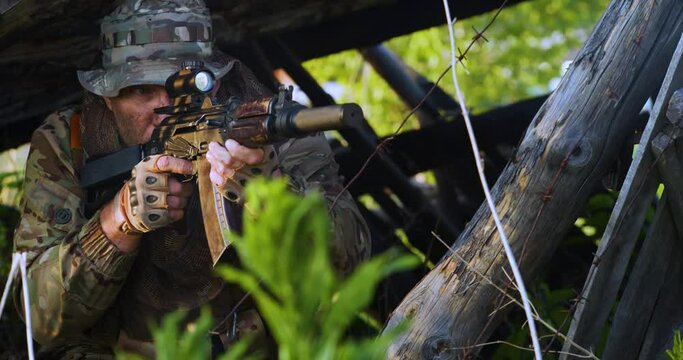 Close-up video of a mercenary soldier fires an automatic rifle from ambush. Special operations of special forces behind enemy lines. Ambush shooting. Slow motion 4k footage.