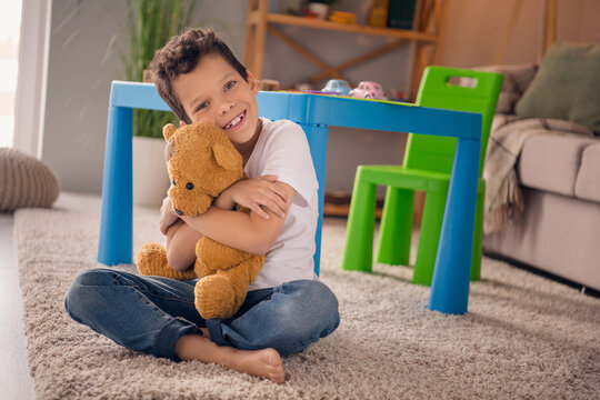 Portrait Of Nice Cheerful Cute Little Boy Sit Floor Embrace Play Favorite Toy Wear White Shirt Light Modern Room Interior Design Apartment