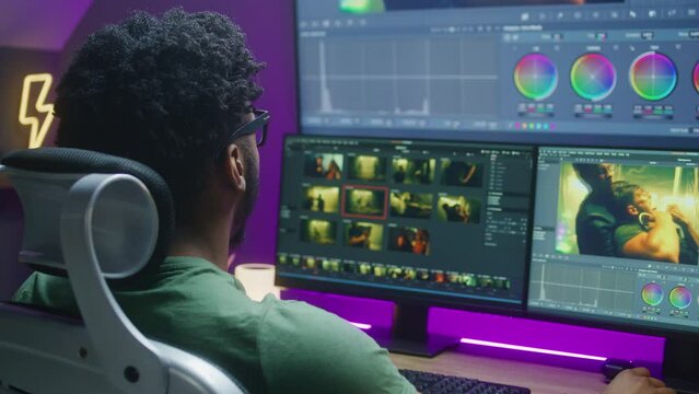 African American video editor makes color grading, works at home office. Action movie footage and program interface on multi-monitor computer and big digital screen. Concept of film post production.