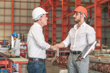 Senior factory owner and engineer staff wearing safety helmets shake hands together to work...
