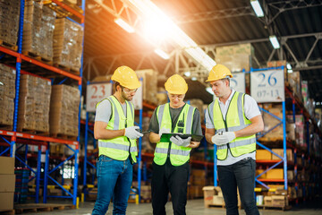 Three warehouse workers using a digital tablet while recording inventory. Logistics employees working with warehouse management software in a large distribution centre.