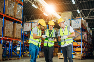 Three warehouse workers using a digital tablet while recording inventory. Logistics employees working with warehouse management software in a large distribution centre. - obrazy, fototapety, plakaty