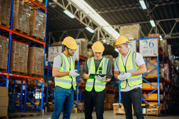 Three warehouse workers using a digital tablet while recording inventory. Logistics employees working with warehouse management software in a large distribution centre.