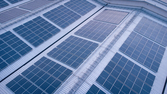 Future green energy and sustainable electricity resource concept. Outdoor focus on solar panels on rooftops or photovoltaics of factories by drone. Industrial roof with solar cell grid with blue tone.