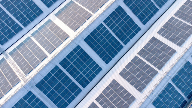 Future green energy and sustainable electricity resource concept. Outdoor focus on solar panels on rooftops or photovoltaics of factories by drone. Industrial roof with solar cell grid with blue tone.
