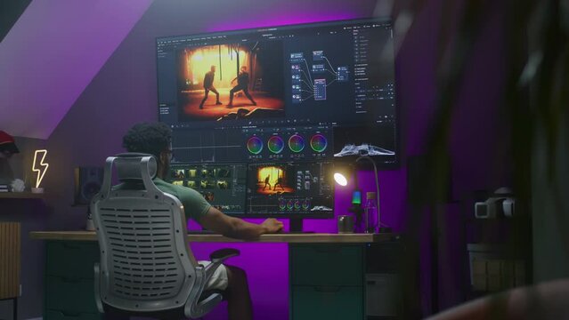 African American colorist edits and makes color grading, works at home. Action movie footage and software interface on multi-monitor computer and big digital screen. Concept of film post production.