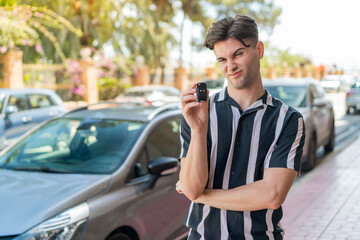 Young handsome man holding car keys at outdoors with sad expression