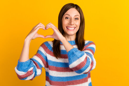 Image of young woman with long brown hair smiling and showing heart shape with fingers isolated over bright background