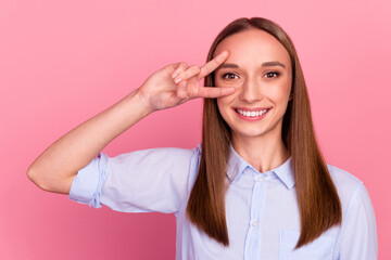 Portrait of young girl shows v sign near eye body language concept over pink backdrop