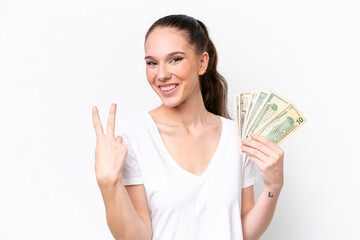 Young caucasian woman taking a lot of money isolated on white background smiling and showing victory sign