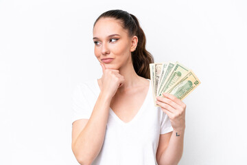 Young caucasian woman taking a lot of money isolated on white background and looking up