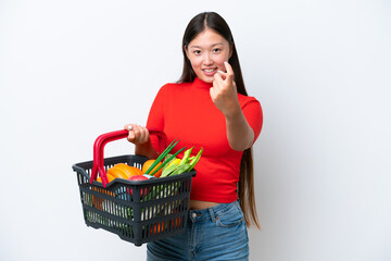 Fototapeta na wymiar Young Asian woman holding a shopping basket full of food isolated on white background doing coming gesture