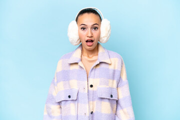 Young Arab woman wearing winter muffs isolated on blue background with surprise facial expression