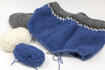 Blue grey white wool yarn knitting on a metal needle with yarn balls on a white background, stockinette stitch knitted texture in progress