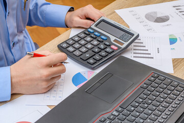 Mężczyzna siedzący przy biurku w pracy, liczący na kalkulatorze , szykujący ofertę dla klienta  - obrazy, fototapety, plakaty