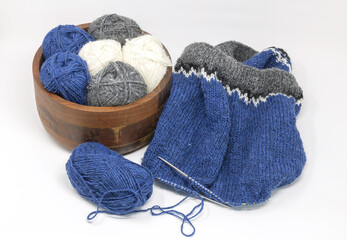 Blue grey white wool yarn knitting on a metal needle with yarn balls in wooden basket on a white background, stockinette stitch knitted texture in progress