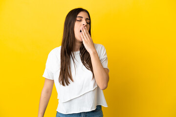 Young caucasian woman isolated on yellow background yawning and covering wide open mouth with hand