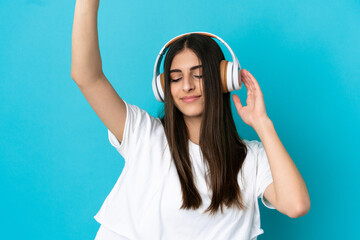 Young caucasian woman isolated on blue background listening music and dancing